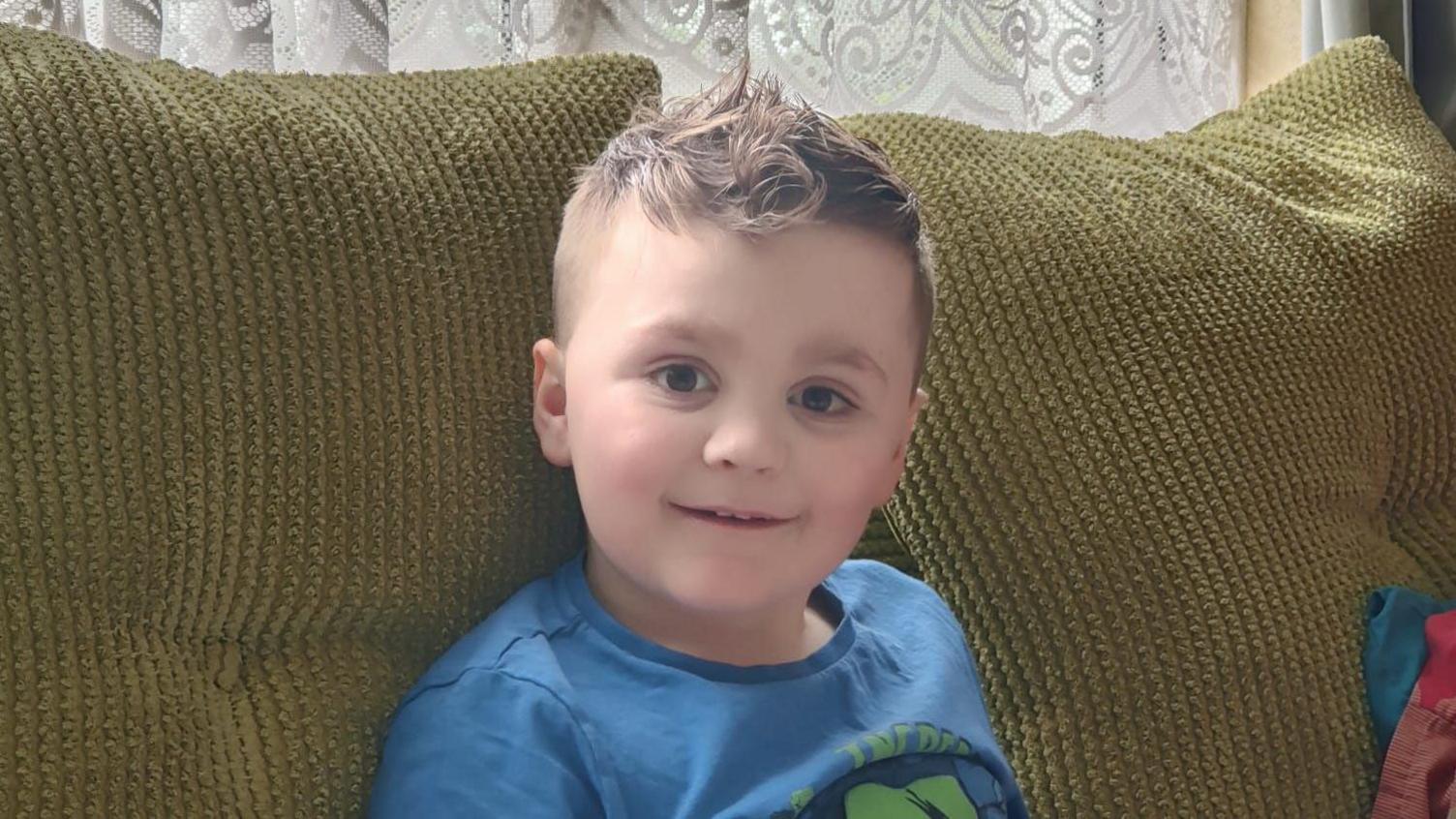 Seven-year-old Max sitting on a sofa and smiling at the camera.