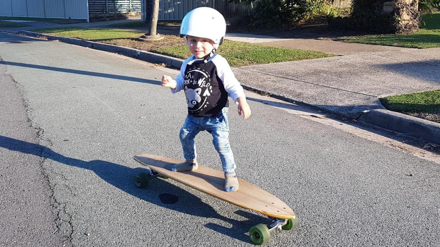 A one-year-old Jaxon Popovic stands on a skateboard