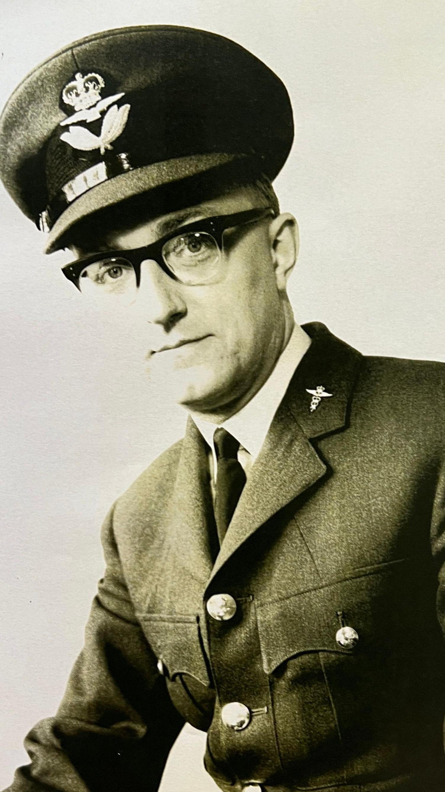 Black and white photograph of a person in military uniform, wearing glasses and a peaked cap with insignia.