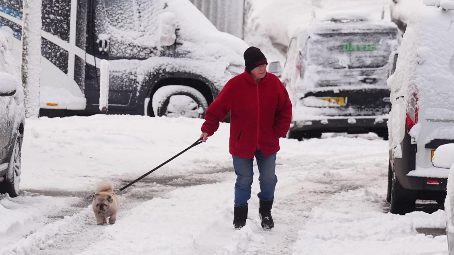 man in red coat walking dog in the snow