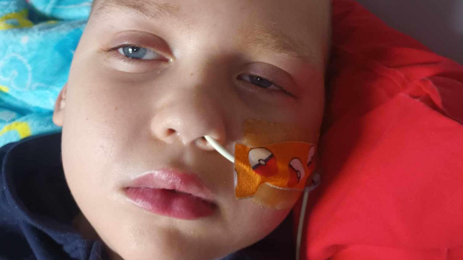 A young boy lying on some pillows. He has a tube coming out of his nose and his eyes are half shut.