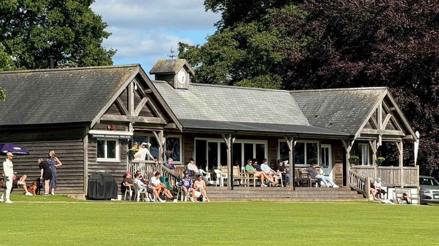 The wooden clubhouse on a sunny day with spectators sitting around the outside