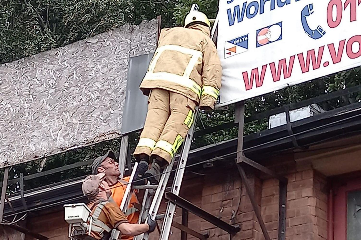 Two workmen approach the hi-vis-clad mannequin using a cherry picker to swap over its clothes.