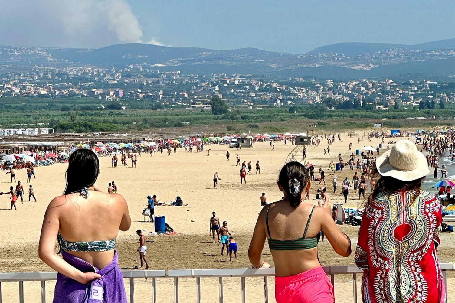 People on a beach with smoke in the distance