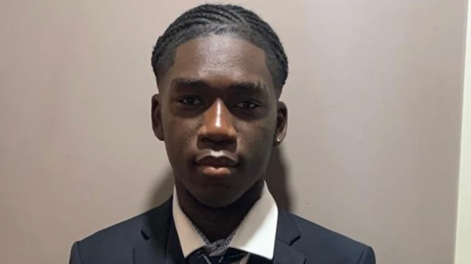 Marcus Fakana in school uniform looks directly at the camera with his head against a grey backdrop.
