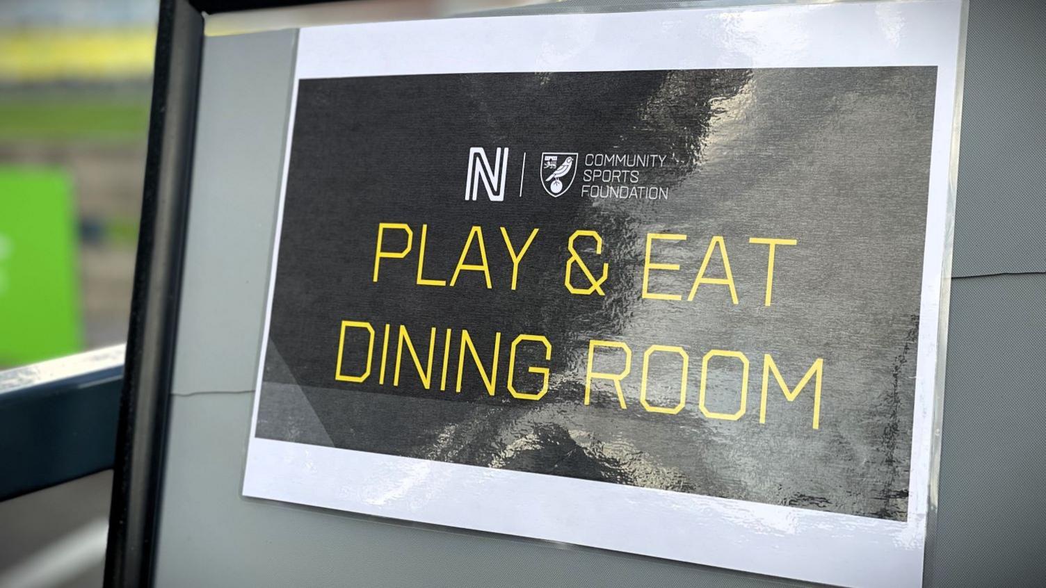 A black sign with yellow writing which says 'play and eat dining room'