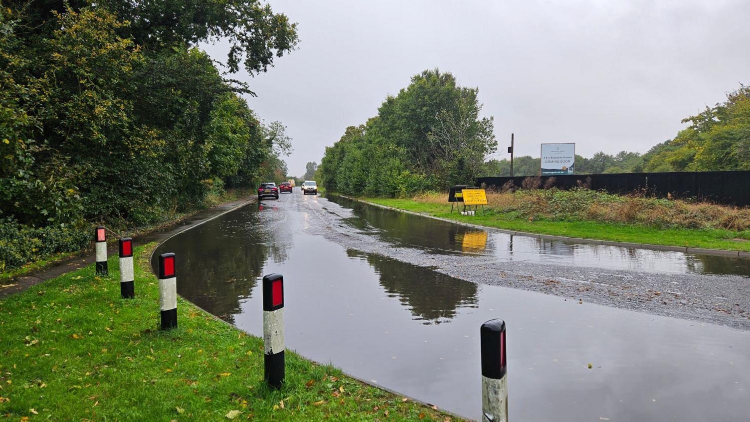 Standing water on the bend of a road in Brampton with approaching cars in the distance