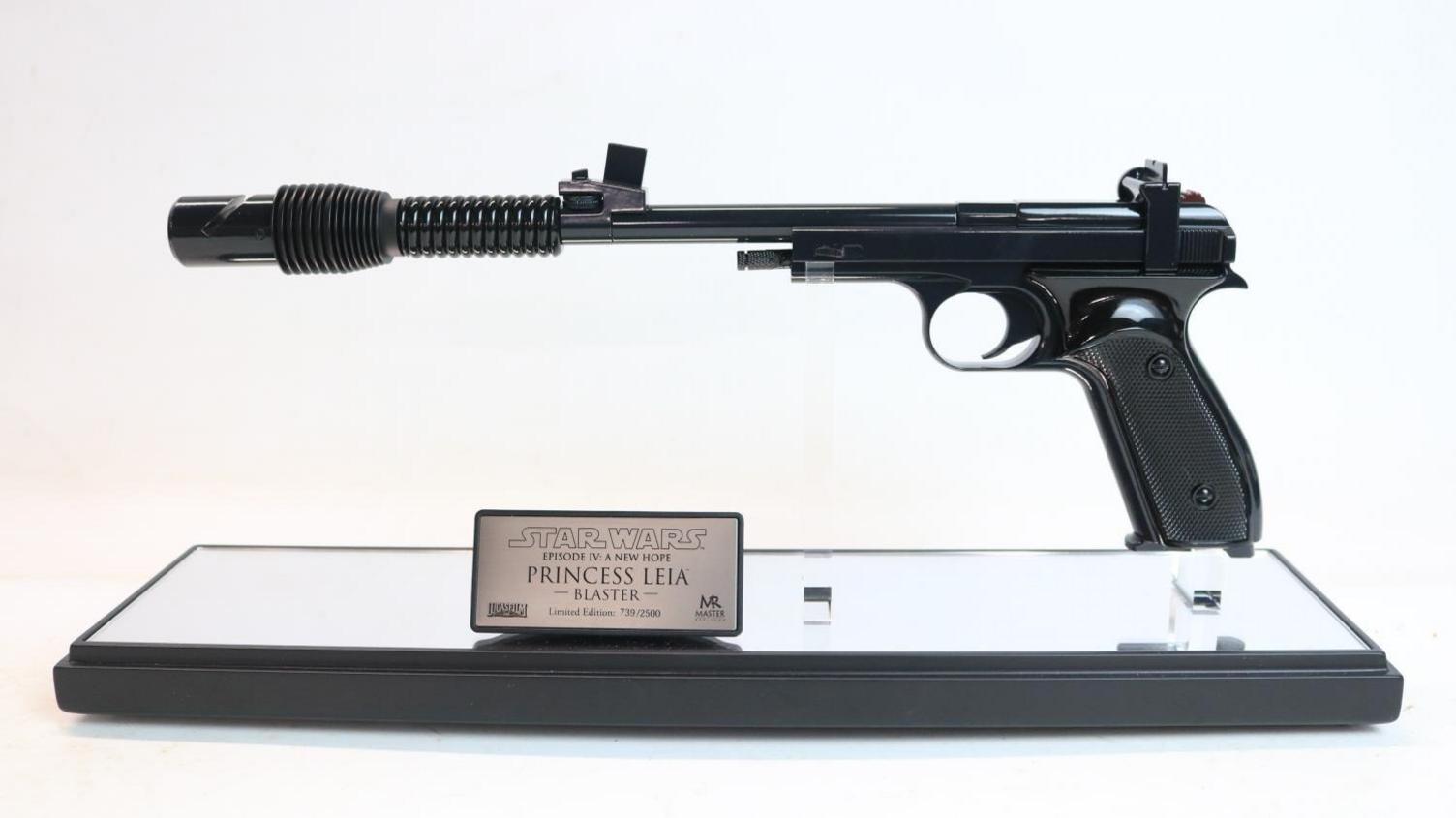 A model futuristic metal gun in a case with a plaque that reads "Princess Leia blaster"