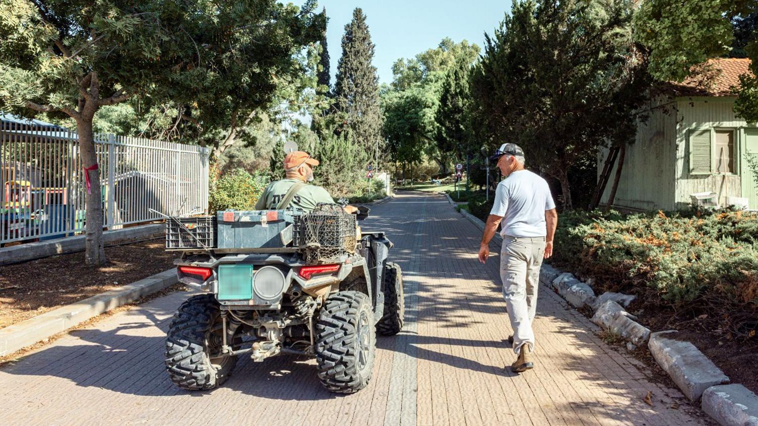 Rami and Simon, both with their backs to the camera. Rami is on an all-terrain vehicle. Simon is walking to the right of him.