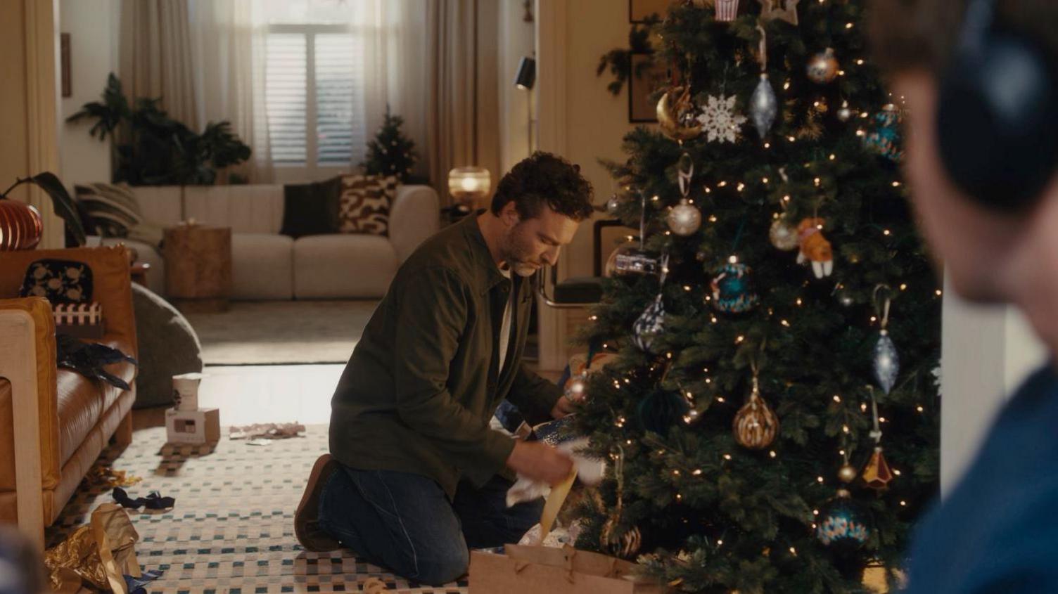 A father opening a present under a Christmas tree, with his son watching