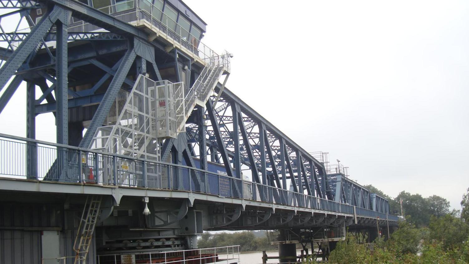 Side view of the dark grey-coloured steel girder bridge with stairway leading up to control tower