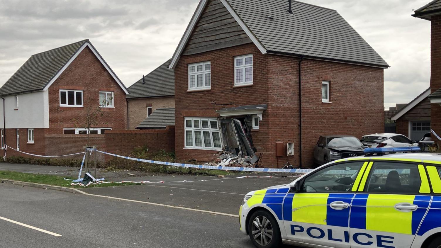 A police car outside the damaged property which has police tape in front of it