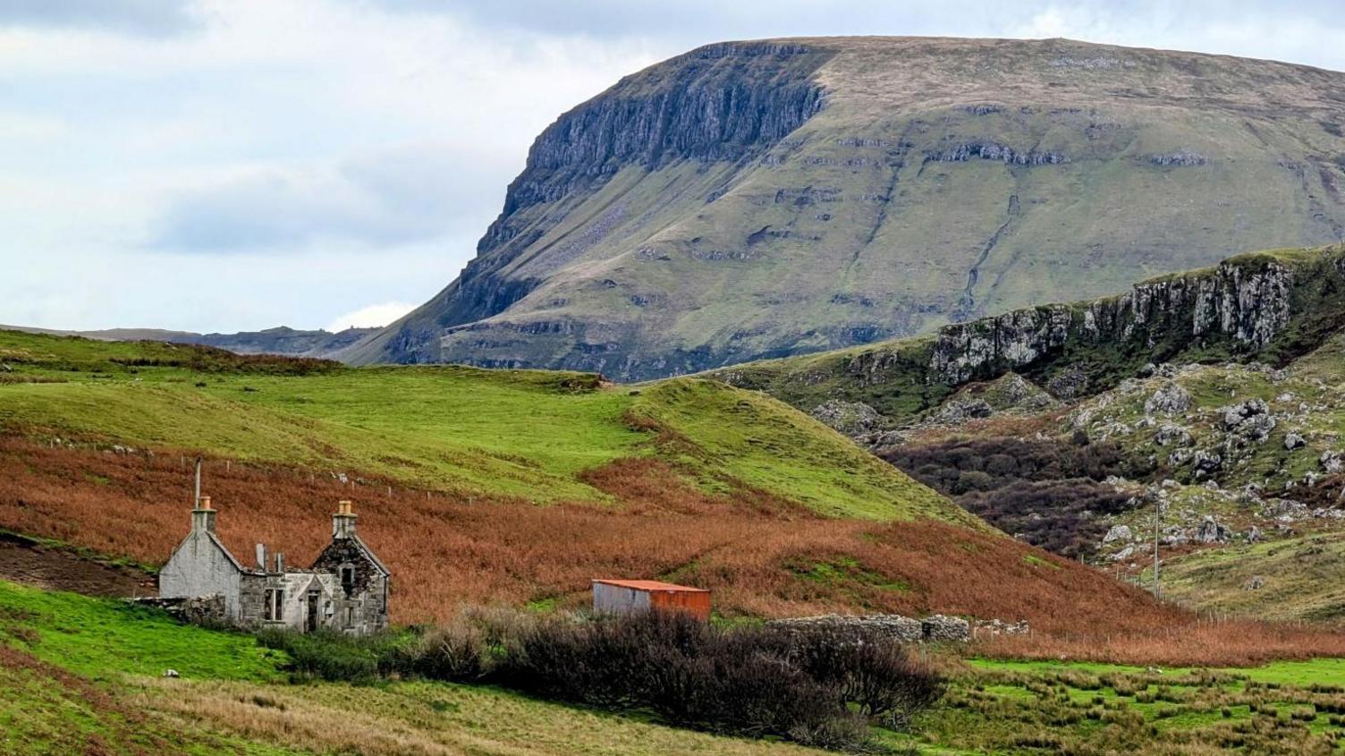 A ruined cottage in a landscape of rocky outcrops and crags.