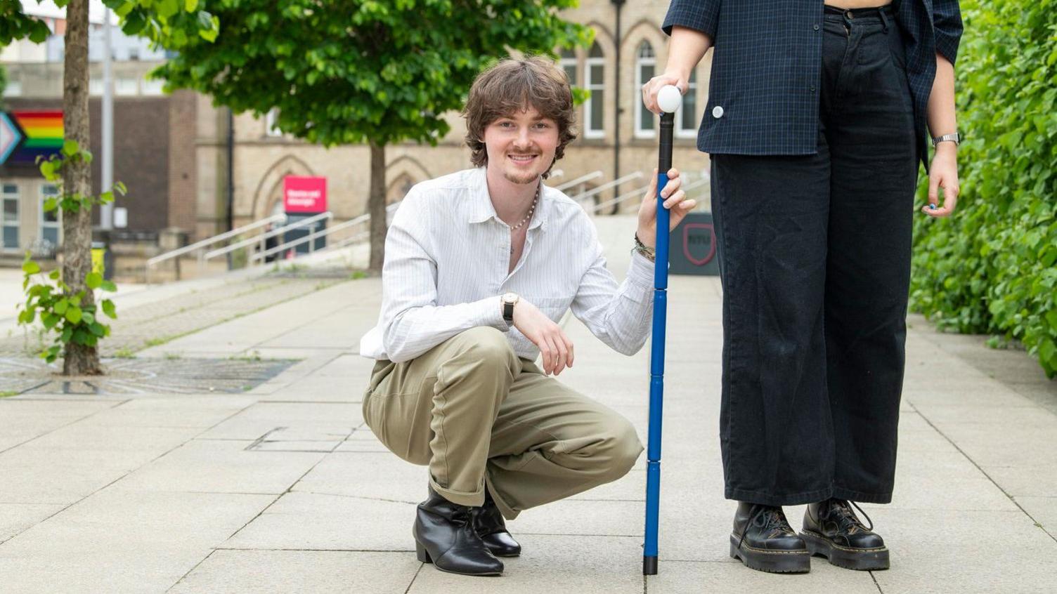 Sean Guyett kneeling next to his walking stick creation