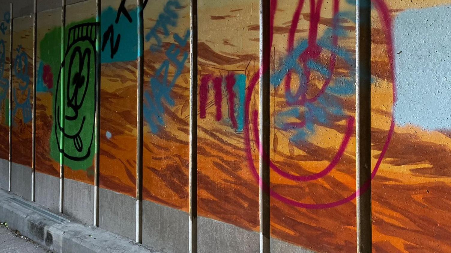 A brown, orange and and yellow mural on a wall, defaced with graffiti.