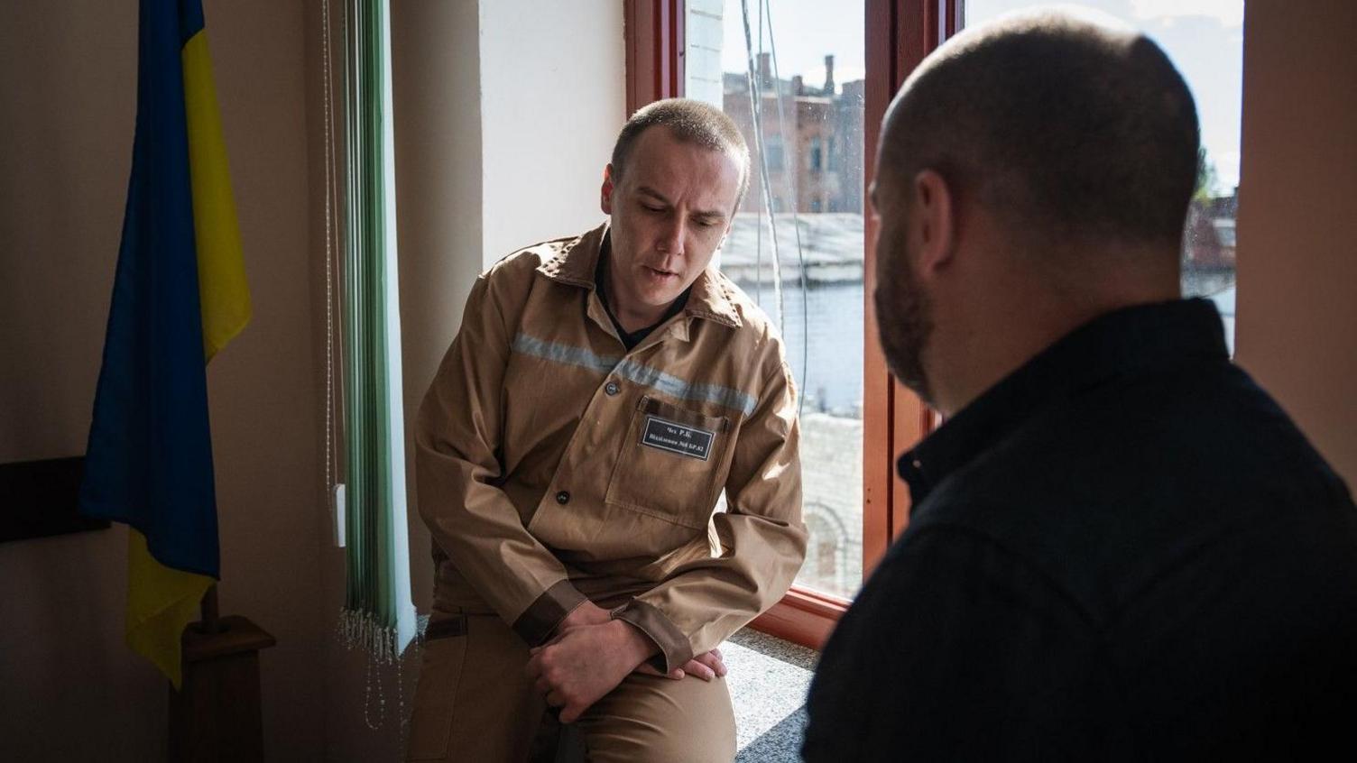 Roman Chech sits on a window sill in his prison uniform, speaking to the BBC's correspondent James Waterhouse