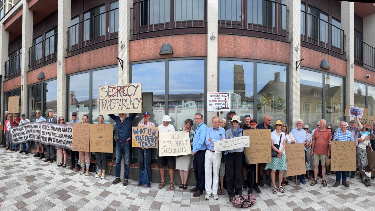 Protestors outside the Cumberland Council building. They are holding various signs saying: "No gas plant dioxins" and the words: "Secrecy Transparency", iwth the words secrecy crossed out.