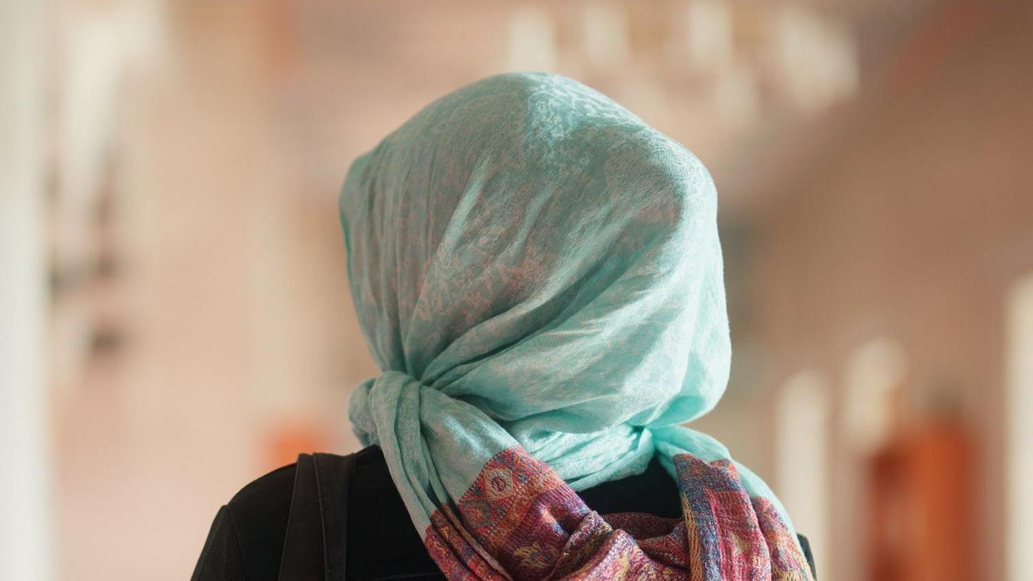 Back of woman wearing a green headscarf in room with several windows.