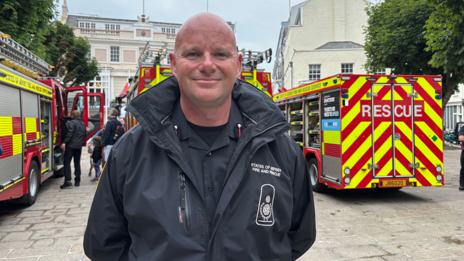 Deputy Chief Fire Officer Bryn Coleman smiles at the camera, there are fire engines behind him