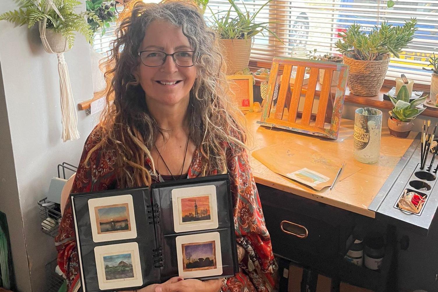 Caroline West sat at her desk holding an album with pieces of her teabag art. 