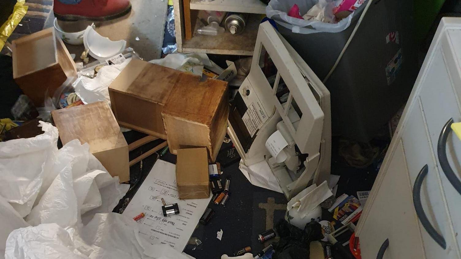More debris on the floor of a shop with draws pulled out of cabinets and their contents emptied everywhere.