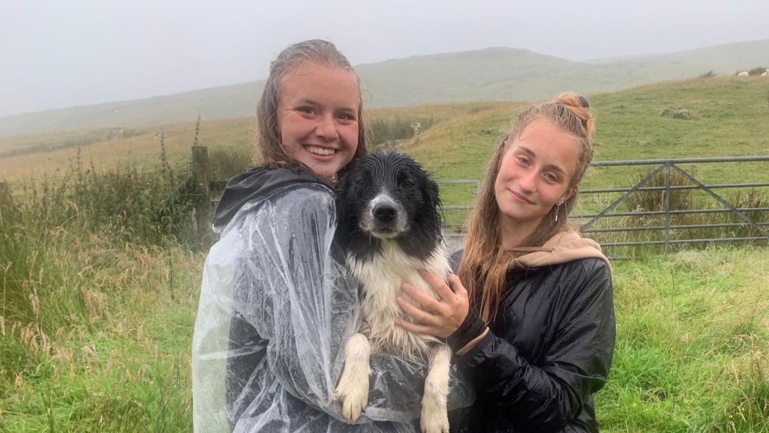 Lucie Kolarikova amd Katerina Mrázková, wearing rain protection, and their dog, Gwaii, near a wet Pen y Fan