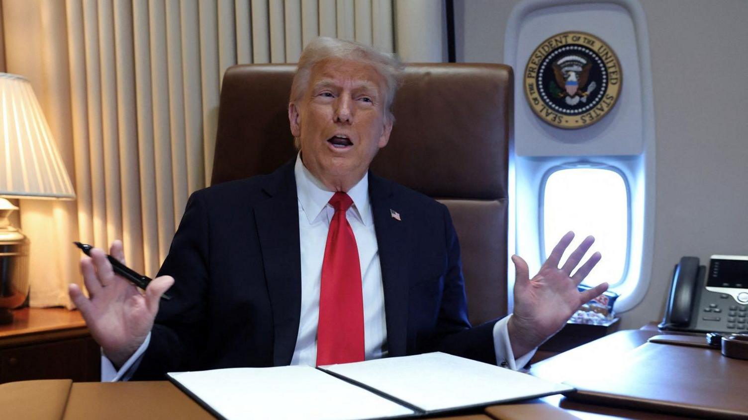 Trump raises his hands as he talks to reporters aboard Air Force One