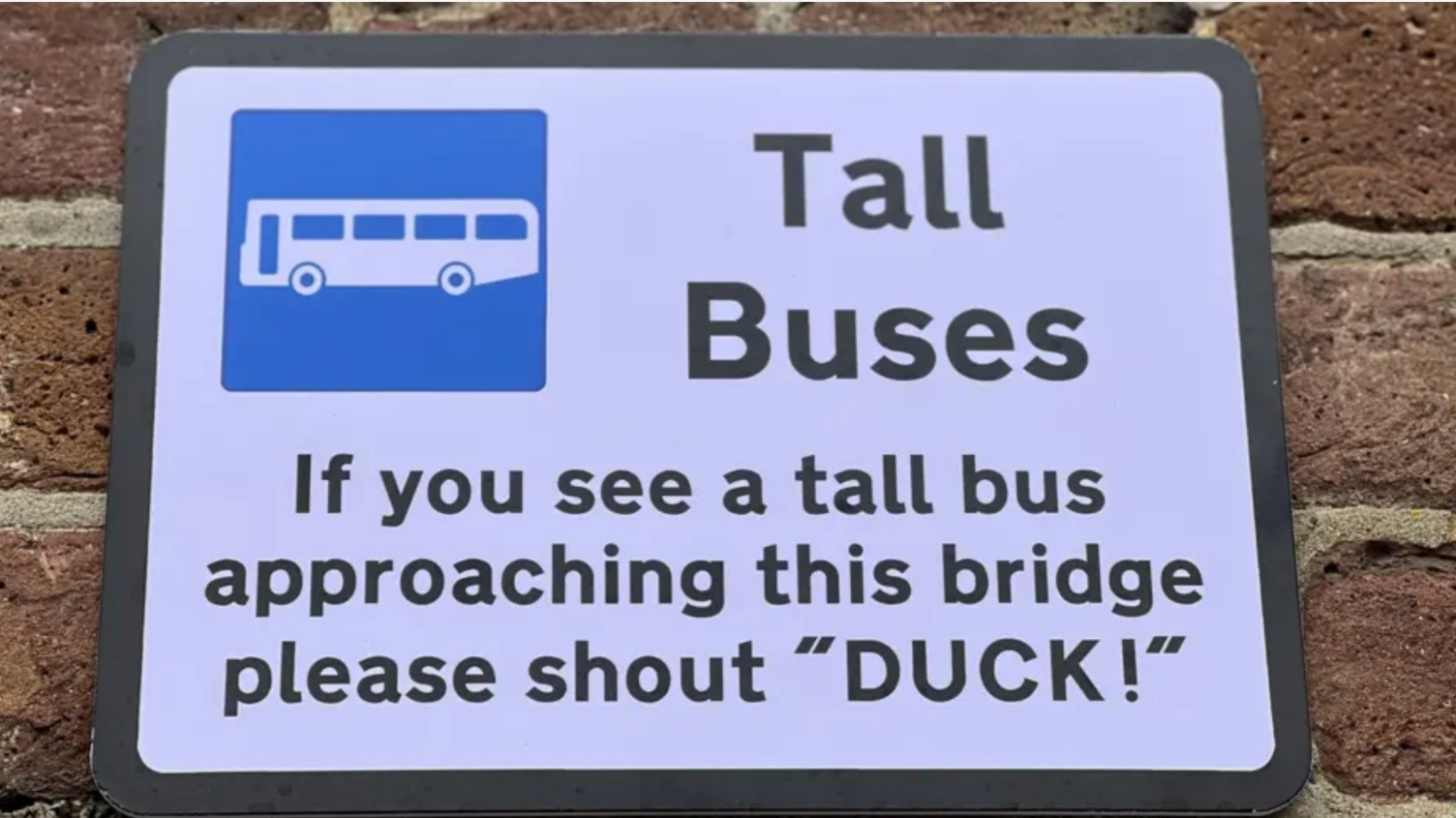 Sign on wall saying "Tall Buses, If you see a tall bus approaching this bridge please shout "DUCK!"