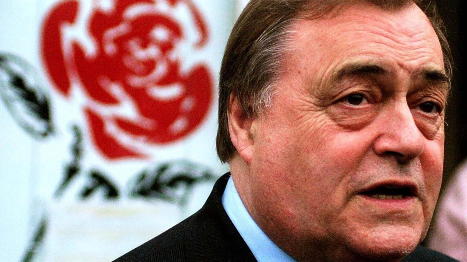 John Prescott, with the red rose emblem of the Labour Party in the background