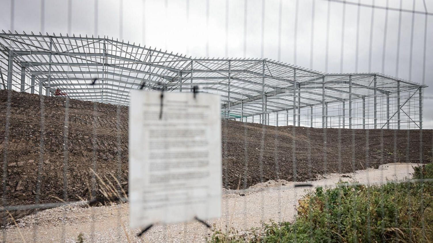 The metal foundations of a giant structure surrounded by grass and dirt. 