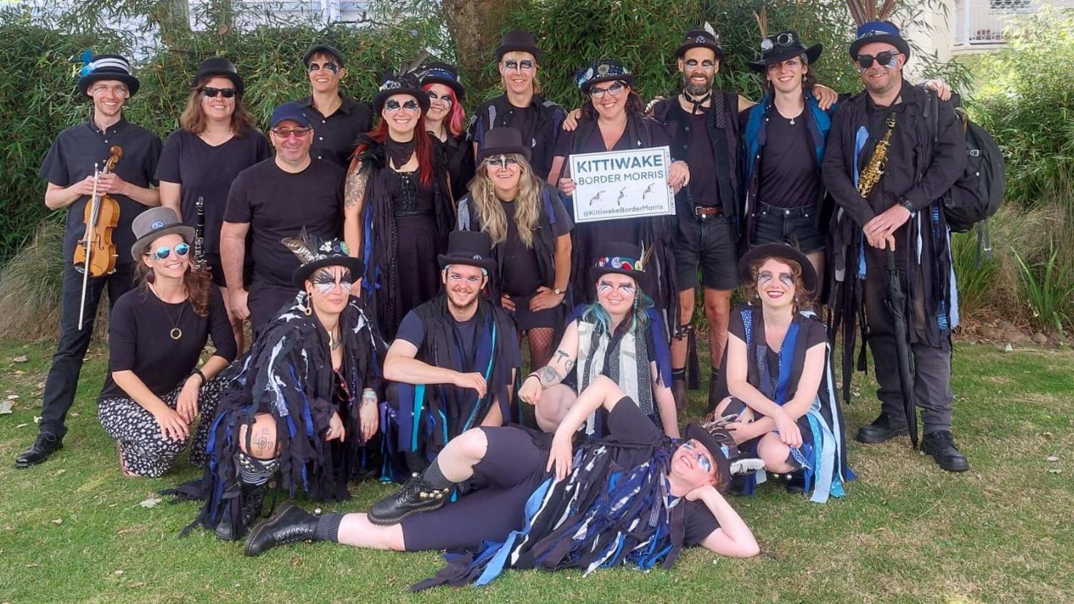 A team photo of Kittiwake on grass. Members are wearing the teams' black outfits adorned with blue rags. 