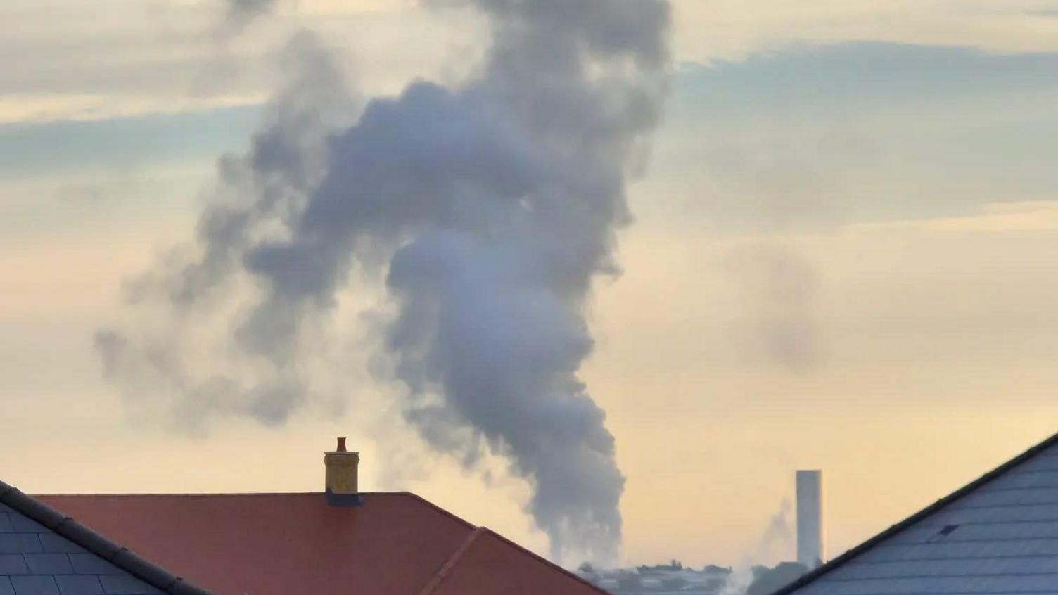 A chimney stack can be seen with a cloud of steam rising high in the sky from it.