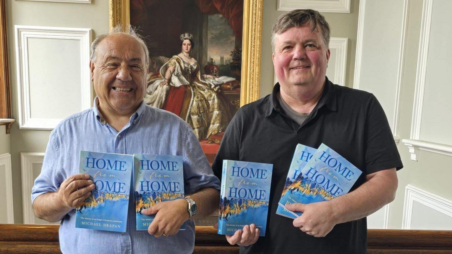 John Lawson and author Michael Drapan holding copies of Drapan's book called Home from Home at Huddersfield Town Hall