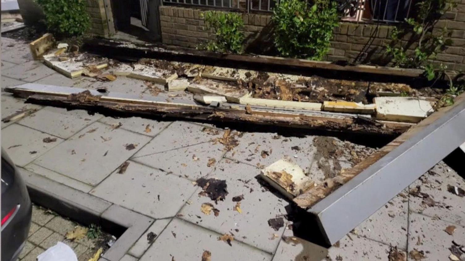 Splintered balcony beams and steel struts on the pavement outside Weavers Quarter, the incident that led to scaffolding around 77 homes and exposed wider design failures.