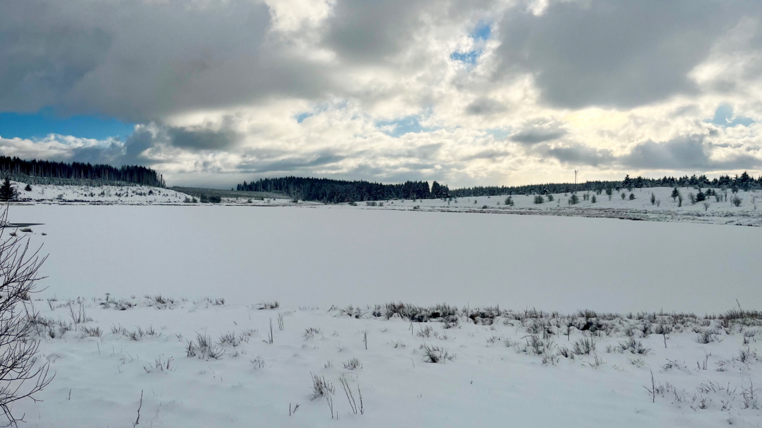 Llyn Bran is a snow-covered and frozen lake, with snow also on fields behind it and in front