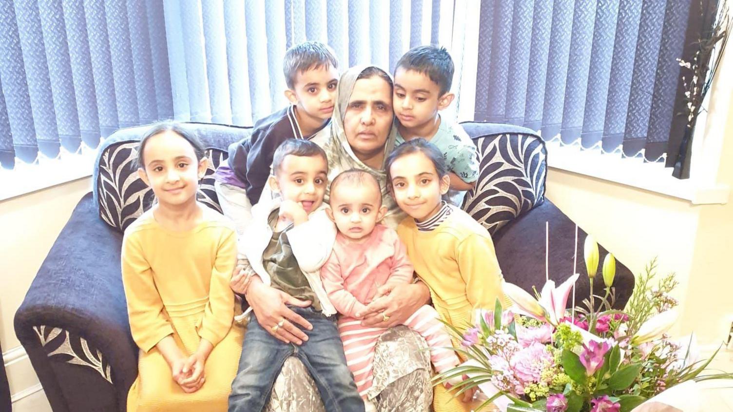 A woman sat on a sofa surrounded by children smiling at the camera