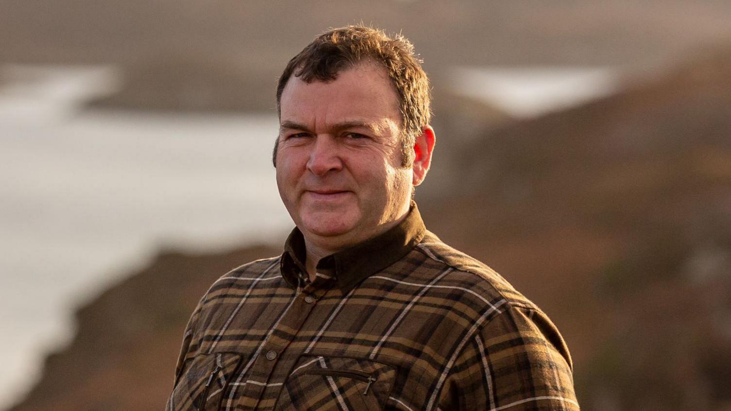 Farmer Donald John Cameron standing in the countryside wearing a check shirt 