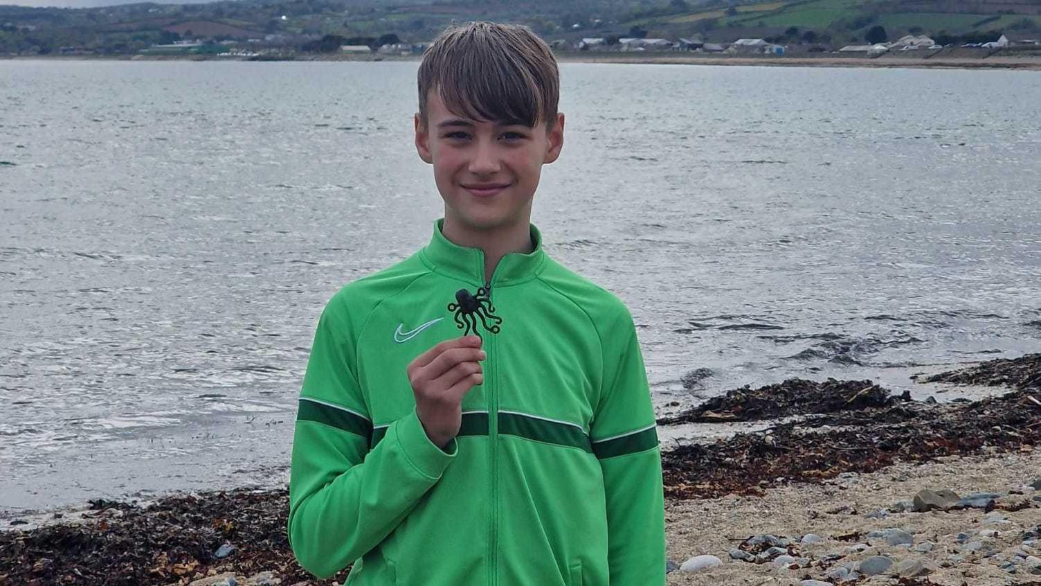 Liutauras is standing on a beach with the sea behind him smiling at the camera as he holds up his Lego black octopus