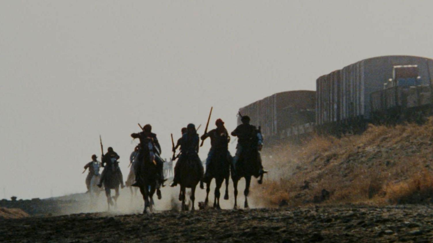 A shot from the film Sholay shows men in silhouettes wielding weapons and riding horses, leaving behind a white film of dust.