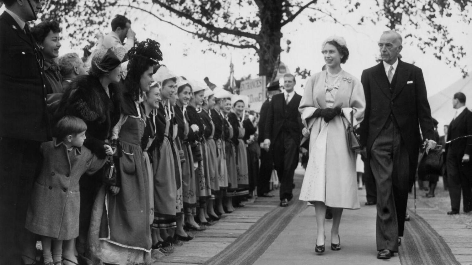 Y Frenhines Elizabeth II yn ymweld â'r Eisteddfod ac yn mynd heibio rhes o gystadleuwyr