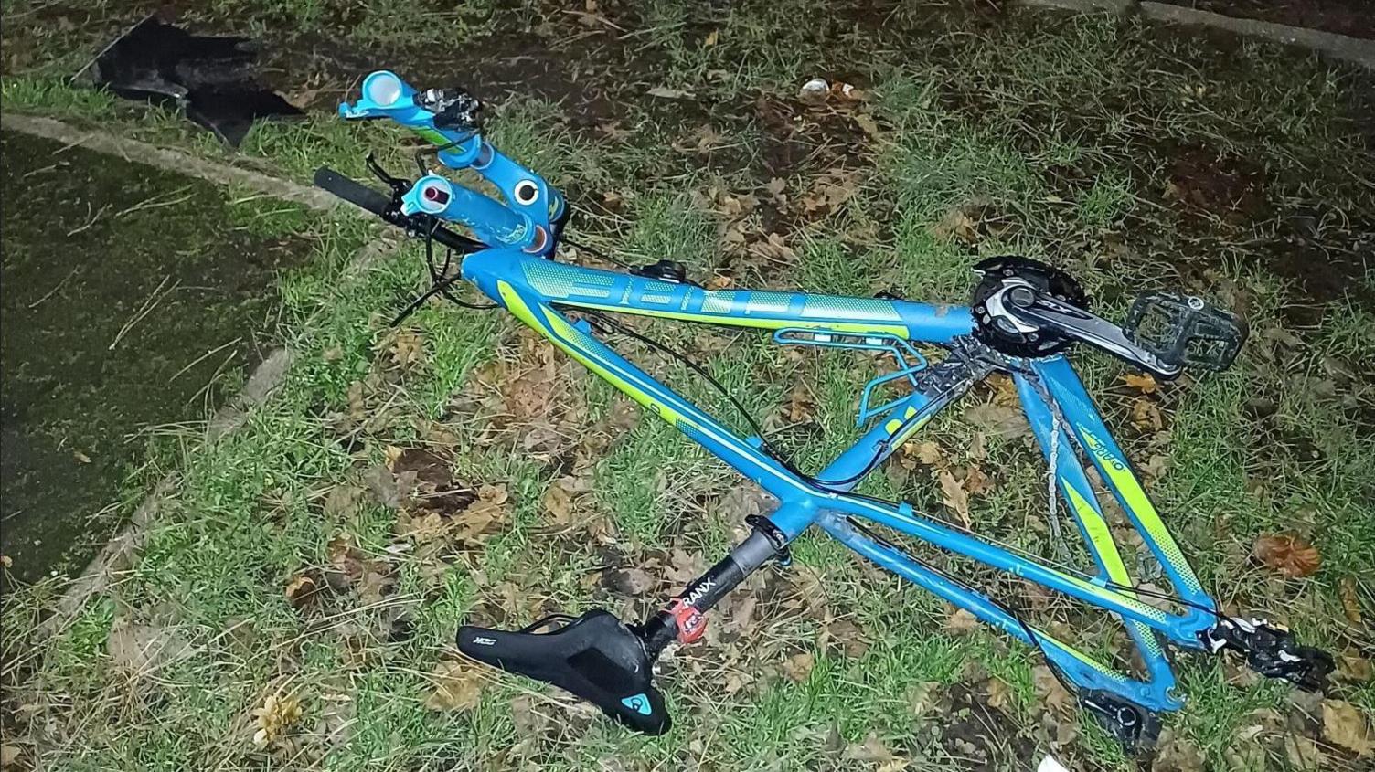 A blue and green bike frame on a grass verge next to a road