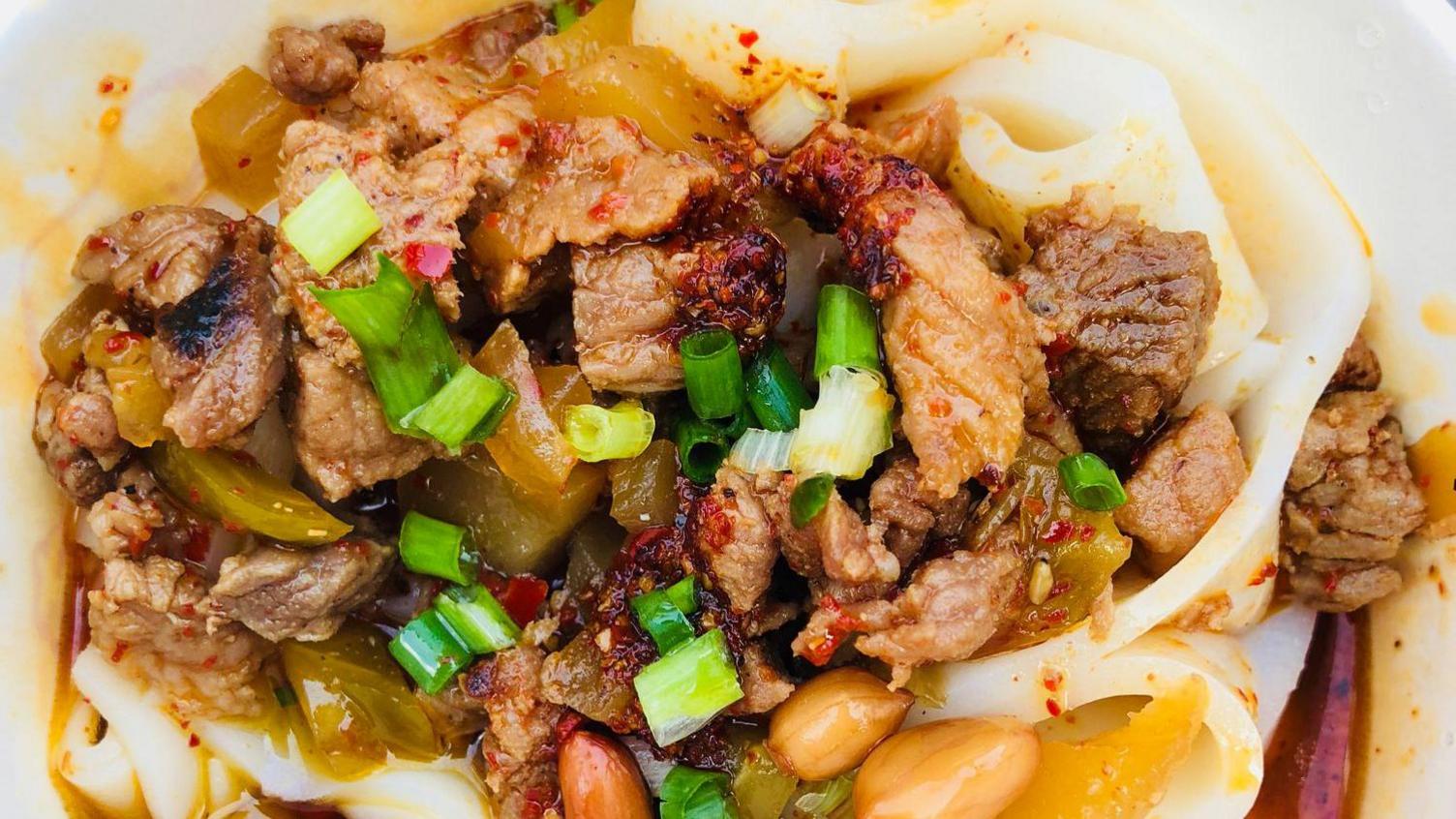 A close-up shot of noodles in chilli oil, topped with meat, peanuts and spring onions