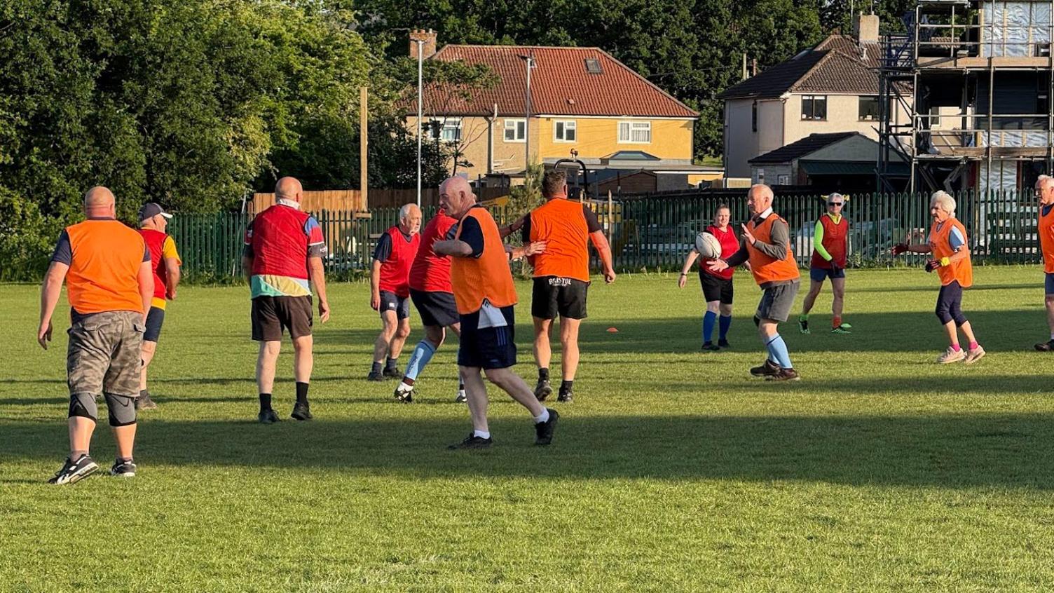 Walking rugby players in brightly coloured orange and red bibs, passing a ball along the line and trying to score.