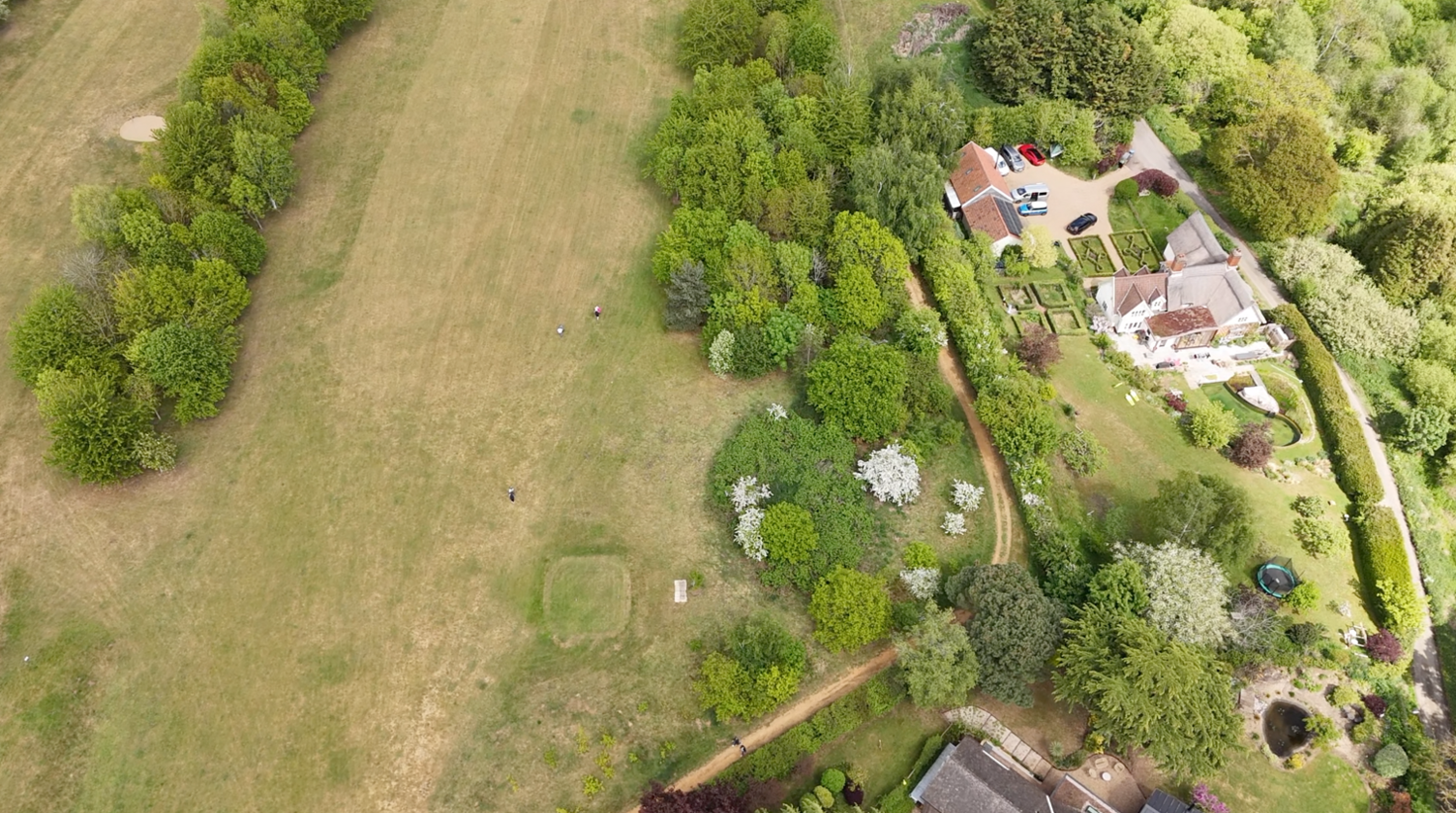 An aerial view of a golf course fairway, lined with trees, and a large house on the right.