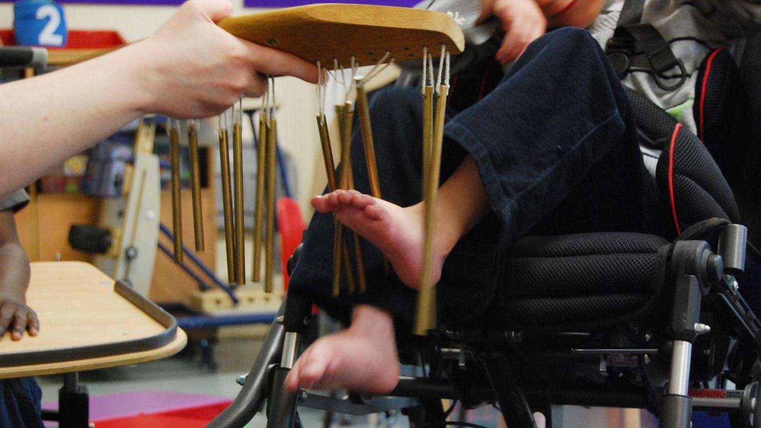 A child in a wheelchair uses their feet to play wind chimes.