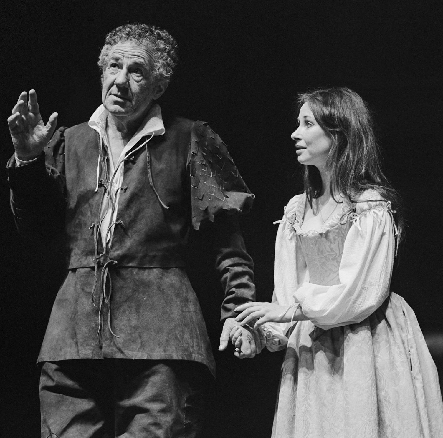 Michael Hordern as Prospero  in rugged dark outfit with arm outstretched and the other being held by Miranda with brown hair and lovingly looking to Hordern in simple outfit