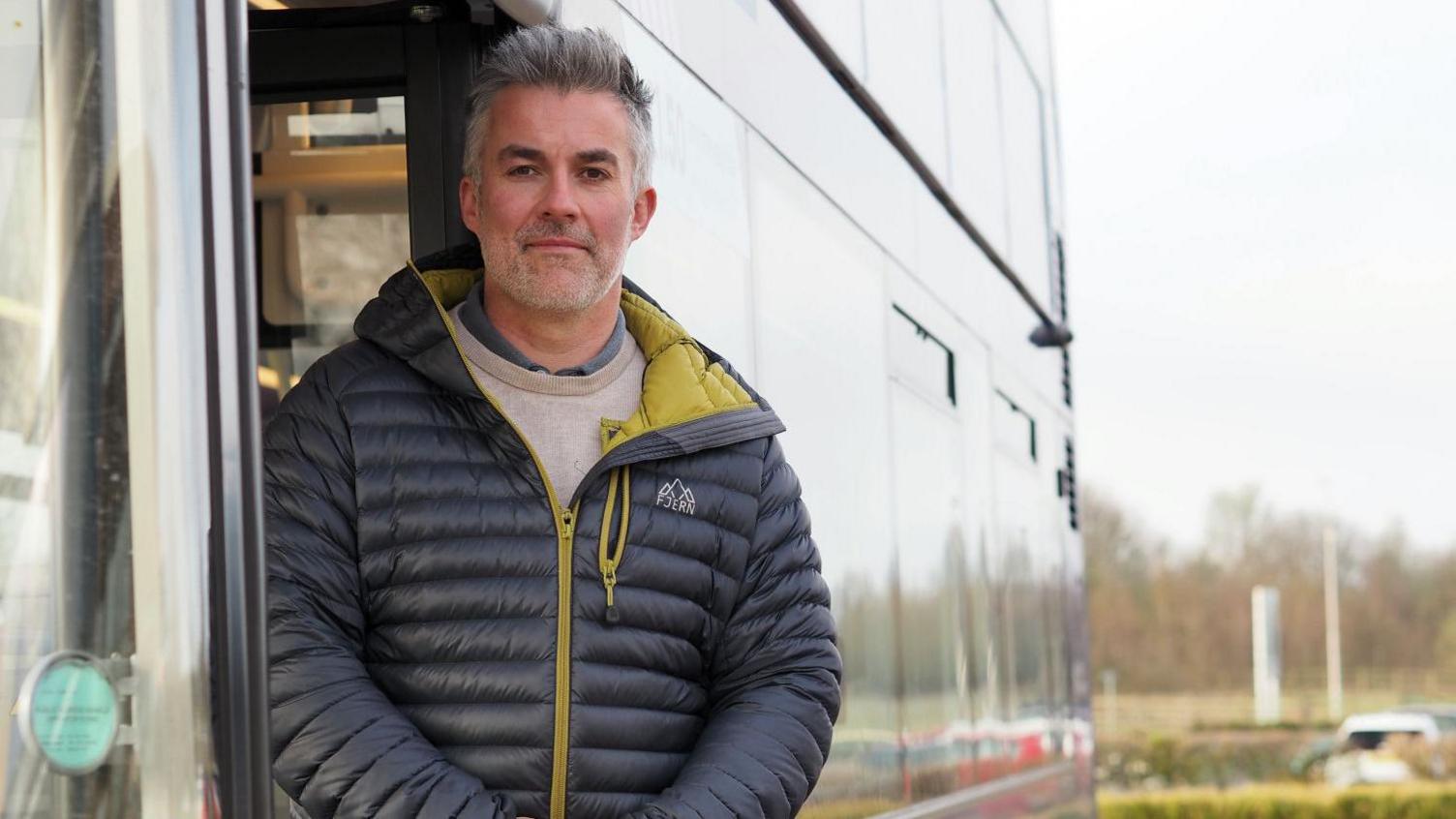The Mayor of York and North Yorkshire David Skaith, who is wearing a puffer jacket, stands in the doorway of a bus.