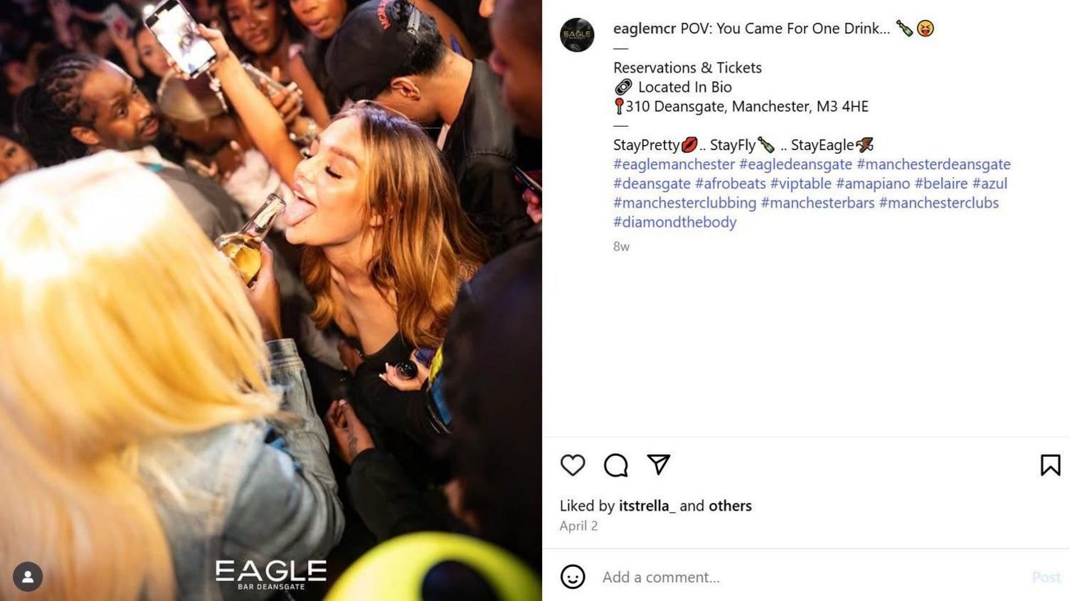 A blonde woman pours a drink into another woman's mouth in a crowded bar