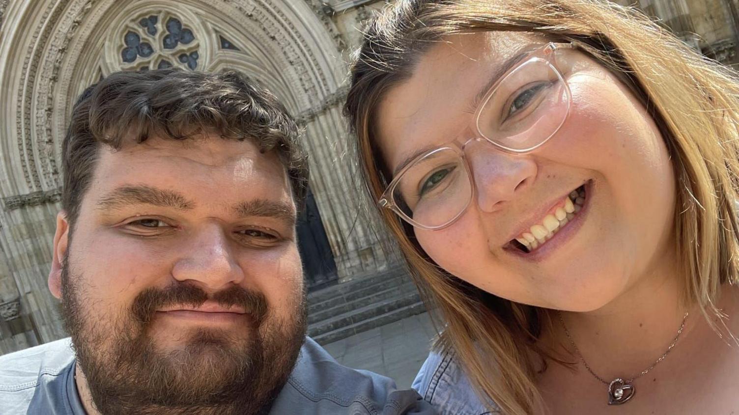 Tom Brakewell and Gabby Evans are smiling in a selfie. Tom has brown hair and a beard and Gabby has shoulder length blonde hair.