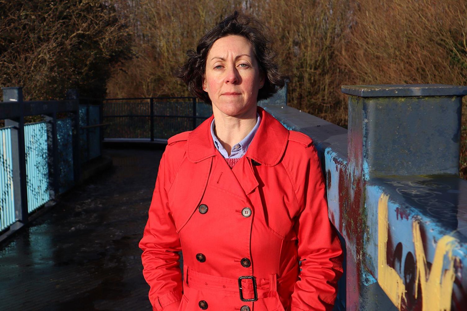 Rowena Pailing standing, in a red raincoat with her arms in her pockets